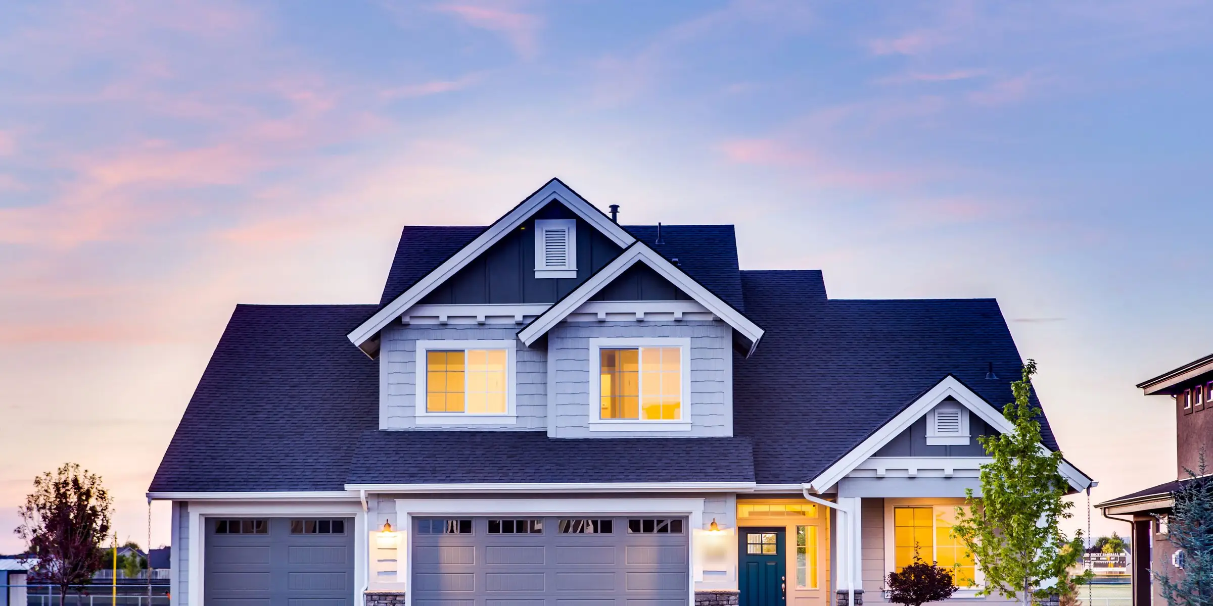 A two-story home at first light, lamps glowing behind its upstairs windows under a pale pink sky.